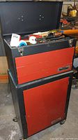 Front view of red and black metal tool locker toolbox with open top chest showing various tools inside