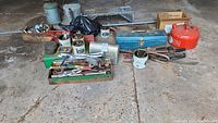 Wide view showing the full assortment of items including various cans, tools, a blue toolbox, and a red gas can on concrete floor.