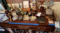 Wide view of lot on wooden table showing trinket boxes, stein, figurines, string art, candle holders, plate.