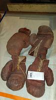 Two brown leather boxing gloves with fabric wrist sections, worn condition, including visible stitching, creases and some discoloration.
