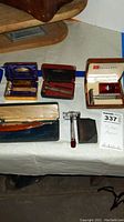 Photo showing multiple vintage razor kits including Gillette and Duran with cases on table.