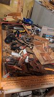 Top view of assorted vintage hand tools spread on a table, including saws, crank drills, and wooden rulers.