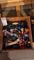 Photo of a box filled with numerous vintage toy cars of various colors and types including trucks and passenger cars.