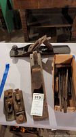Three vintage woodworking hand planes displayed on a table with one tagged with lot number, showing metal and wood construction and worn condition.