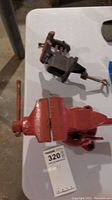 Large red metalwork vise angled to show jaws and handle on white tabletop