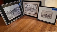 Three framed wall art pieces, including sketches by Thomas Malloy and Cincinnati Roebling Bridge, arranged leaning against a wall on wood floor.