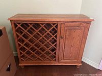 Front view of wood bar cabinet showing lattice style wine bottle storage on left and paneled cupboard door on right.