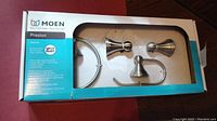 Box front showing Moen brand, Preston series, and visible bath hardware items inside box