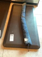 Two black foam chef mats and one fabric door snake placed on the floor in front of a kitchen cabinet, showing full view of mats and door snake with patch and string.