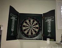 Front view of opened dart board cabinet mounted on the wall with scoreboards on inside of cabinet doors