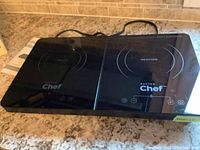 Top view of the black glass double induction cooktop showing two heating zones and touch control buttons, with 'Master Chef' branding.