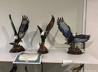 Photo showing all three eagle figures displayed side by side on a shelf with one certificate of authenticity in front