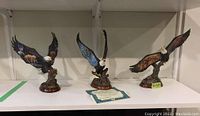 Three eagle figurines on a white shelf with two COAs placed in front of them, showing size and condition from front view.