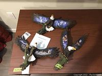 Top view of three Robin Koni eagle figures on a table, showing detailed painted wings and COA booklet.