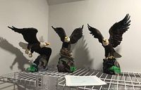 Photo of three eagle figurines on a metal shelf, each posed in different flight or perch positions, with visible green tags and a Certificate of Authenticity.