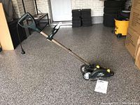 Full view of the Yard Works electric lawn edger showing metal shaft, black and green wheel housing, handles, and power cord on garage floor.