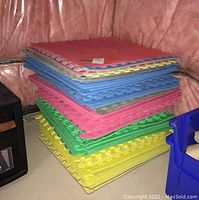 Stack of interlocking foam floor mats in red, blue, pink, green, and yellow colors, neatly stacked against a pink plastic-covered wall.