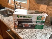 FoodSaver FM5300 Series vacuum sealing system box on countertop showing product branding and picture of vacuum sealer device with packaged meat sample.