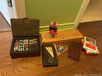 Full display of lot contents including wooden domino box opened, cribbage boards, decks of cards, magic cube, and peg game arranged on a wooden surface.