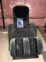 iJoy-100 UPS green massage chair with remote control and manual seen on seat, fabric upholstery in basement storage area.