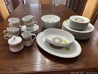 Full set from a distance on table showing stacked plates, bowls, cups, serving pieces.