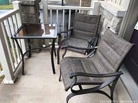 Photo showing two patio chairs and one metal and glass top square table together on concrete patio by a house entryway.