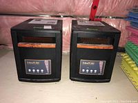 Two black EdenPure GEN3 portable heaters side by side in a basement setting with visible pink insulation and foam mats nearby.