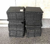 Stacks of black resin interlocking floor tiles, showing multiple piles organized and ready for use.
