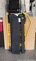 Folded safety ladder/scaffolding unit showing yellow frame and black platforms with wheels visible.