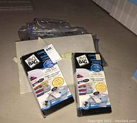 Two unopened Space Bag 5 bag combo sets with packaging placed on floor alongside loose vacuum storage bags and two beige fabric storage bags.