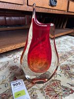 View of the teardrop shaped clear and red art glass vase sitting on floral patterned carpet in front of wooden furniture.