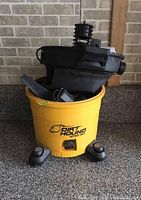 Front view of yellow Dirt Hound wet/dry vacuum with control and nozzle visible on top. Unit on wheeled base.