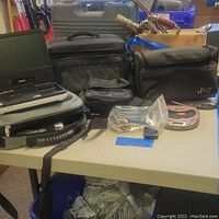 Lot containing 3 camera bags, Kodak Tele-Disc camera, small camera accessory device, and accessories in plastic bags on table