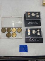 The two US Mint Silver Proof Sets for 1992 and 1994 alongside a clear plastic case containing six large commemorative coins. Coins are visible with clear detailing on the proof sets and embossed imagery on commemoratives.