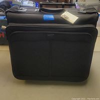 Front view of black garment bag suitcase showing zippered front compartments and handle on top.