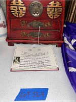 Close-up of red jewelry box with brass locks and floral decorations, certificate shown in front.