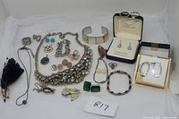 Full lot showing mixed jewelry: earrings, bracelets, rings, necklaces, and pins arranged on white background.