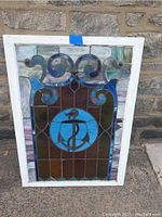 Full view of the stained glass panel showing the anchor theme in blue and surrounding colorful glass with white frame.