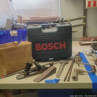 Bosch carrying case with planer, hand planes, files, chisels, adjustable wrench, hand drill and other hand tools on table.