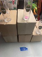 Five stacked cardboard boxes with several tall clear glass beer mugs placed on top, each featuring the green Erbacher logo label with crown emblem.