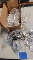 Box filled with various new metal belt buckles and parts individually bagged.