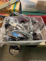 Plastic bin filled with multiple G by Guess belts, all individually wrapped in clear plastic packaging.