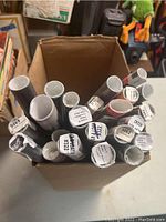 Top view of cardboard box filled with rolled posters labeled with names and numbers such as Tupac and other film titles.