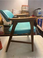 Side view of mid century modern chair showing turquoise vinyl seat and backrest with wooden armrests and legs.