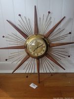 Full view of the vintage atomic starburst clock with wooden and brass spokes on a white wall.
