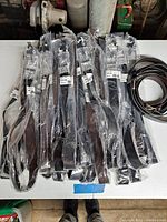 Overview of multiple new, mostly black Guess belts in sealed plastic packaging and a few unwrapped belts.