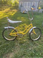Side profile of the yellow Schwinn Sting Ray bike with white banana seat outdoors on grass.