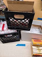 Black plastic crates and cardboard boxes used to store and organize the pipe cleaners and coin bags.