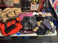 Overview of lot showing various bags in different styles including designer and non-designer handbags and purses in multiple colors and materials