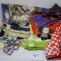 Lot containing six scarves with various designs and colors, leather metal bracelets, and beaded belt buckles on display.